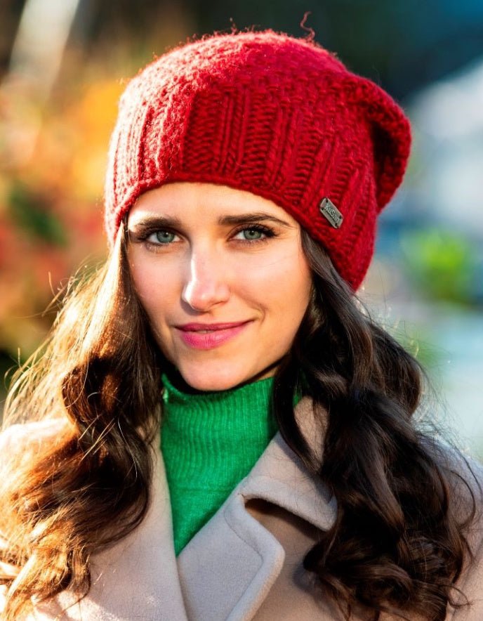 Woman wearing a red knit beanie and green sweater with a blurred outdoor background
