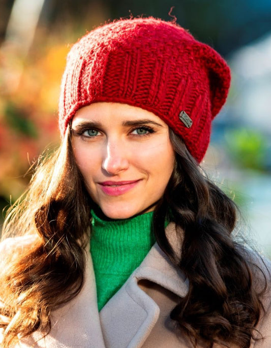 Woman wearing a red knit beanie and green sweater with a blurred outdoor background