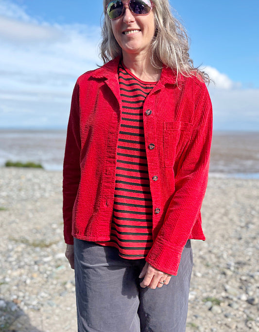 Person wearing a red jacket cord shirt over a red and black striped shirt on a beach