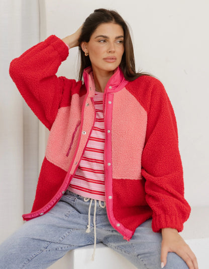 Woman wearing a red and pink jacket with a striped shirt and jeans on a white background