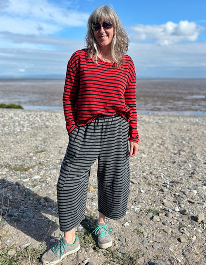 Person wearing a red and black striped shirt and black and gray striped pants standing on a pebbly beach.