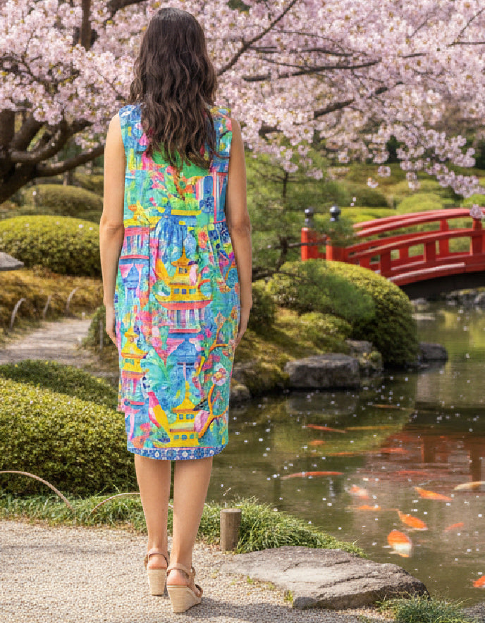 Woman in a colorful dress standing in a Japanese garden with cherry blossoms and a red bridge.