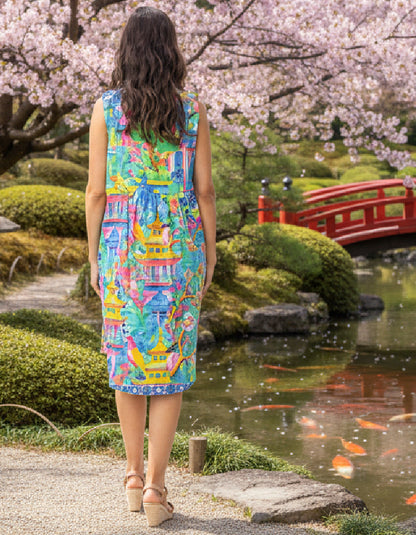 Woman in a colorful dress standing in a Japanese garden with cherry blossoms and a red bridge.