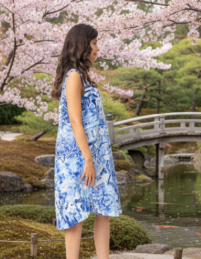 Woman in a blue dress standing in a cherry blossom garden with a bridge in the background