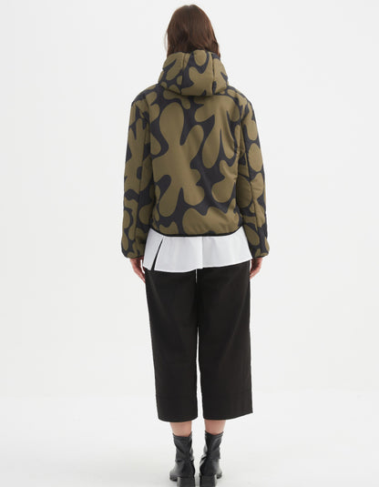 Woman wearing a camouflage olive and black reversible puffer jacket on a white background