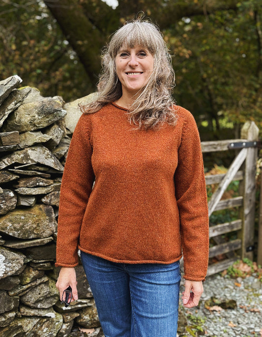 Woman wearing a brown sweater standing in front of a stone wall and wooden gate.