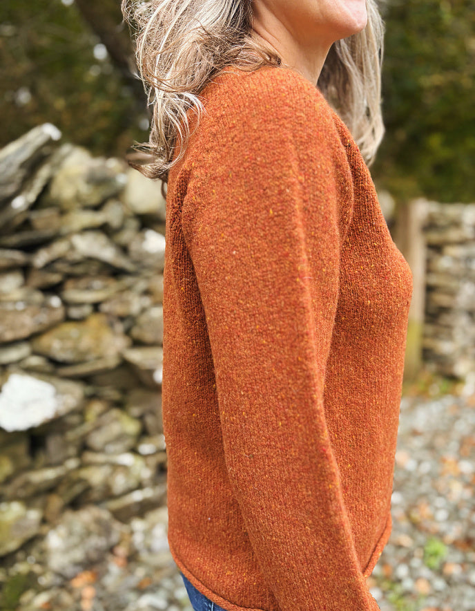 Person wearing a rust-colored sweater standing in front of a stone wall.