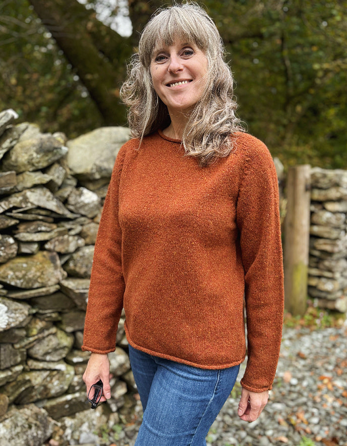 Woman wearing a rust-colored sweater standing in front of a stone wall.