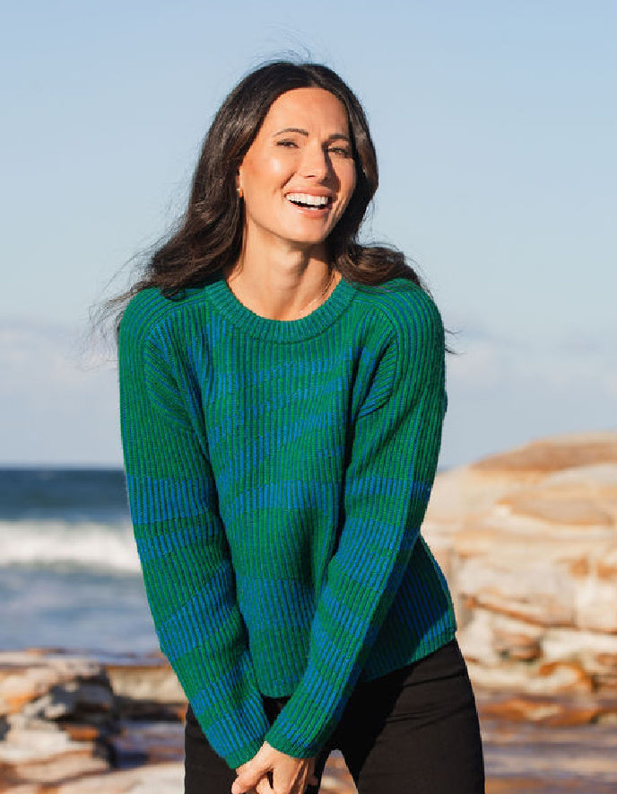 Woman wearing a green and blue sweater standing on a beach with ocean waves in the background