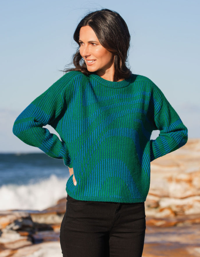 Woman wearing a green sweater standing on a beach with ocean waves in the background