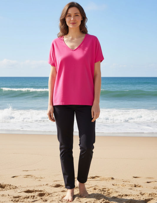 Woman wearing a pink top and black pants standing on a beach with ocean in the background
