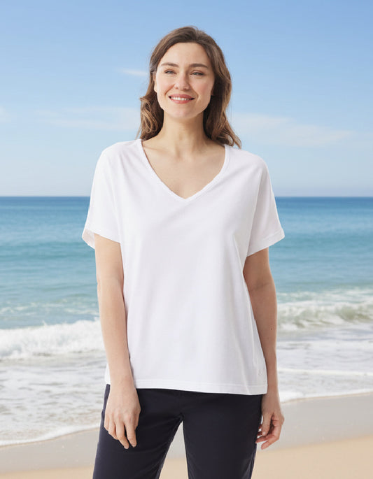 Woman wearing a white t-shirt and black pants standing on a beach with blue ocean and sky.