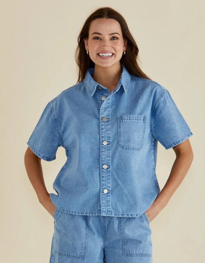 Woman wearing a blue denim shirt and shorts on a beige background