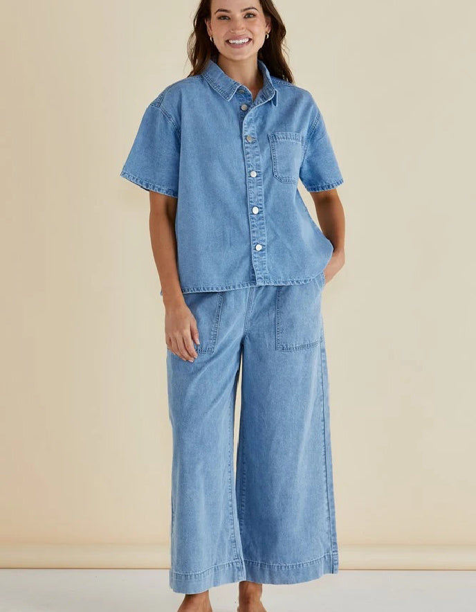 Woman wearing a denim outfit with a short-sleeve shirt and wide-leg pants against a beige background
