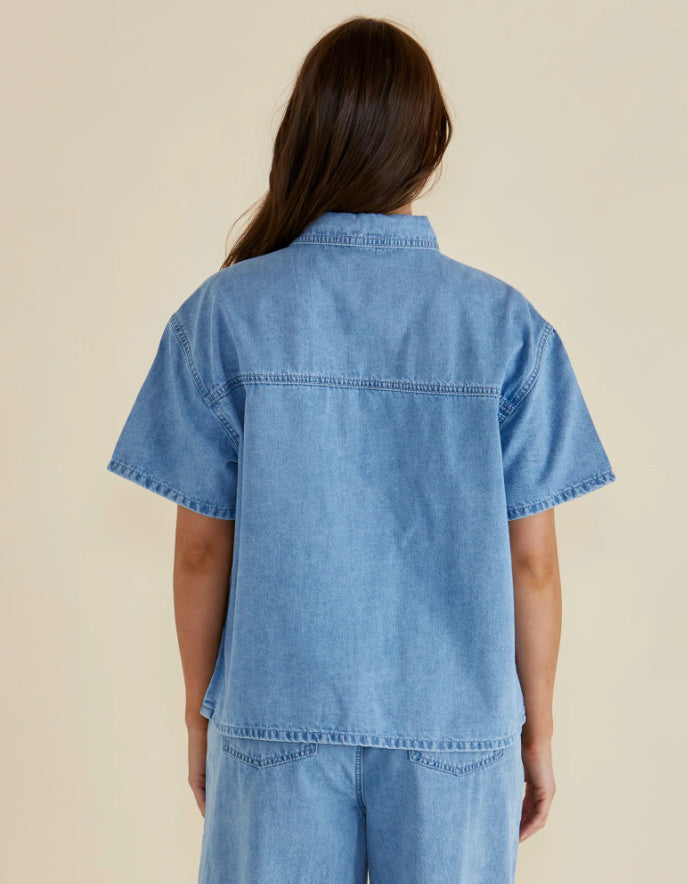 Person wearing a light blue denim shirt and pants on a beige background