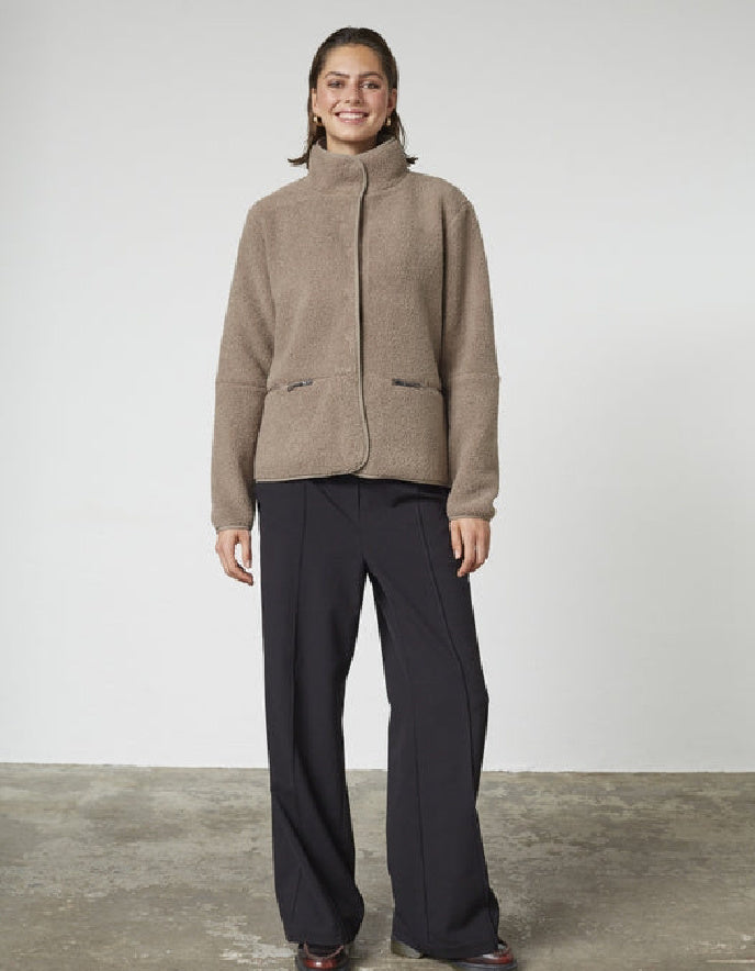 Person wearing a brown jacket and black pants against a white background