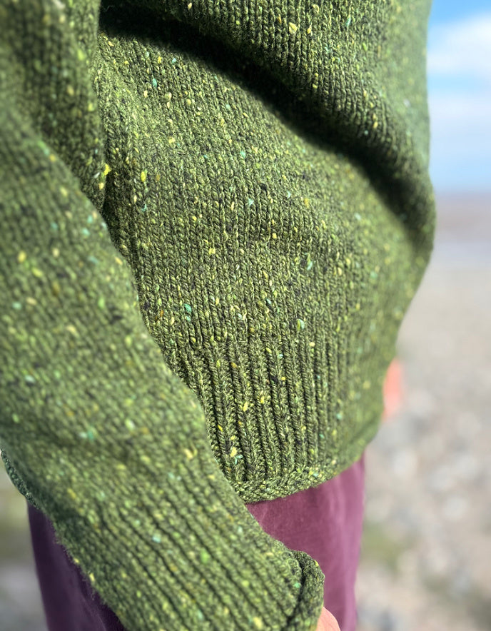 Close-up of a green knitted sweater sleeve with a blurred background