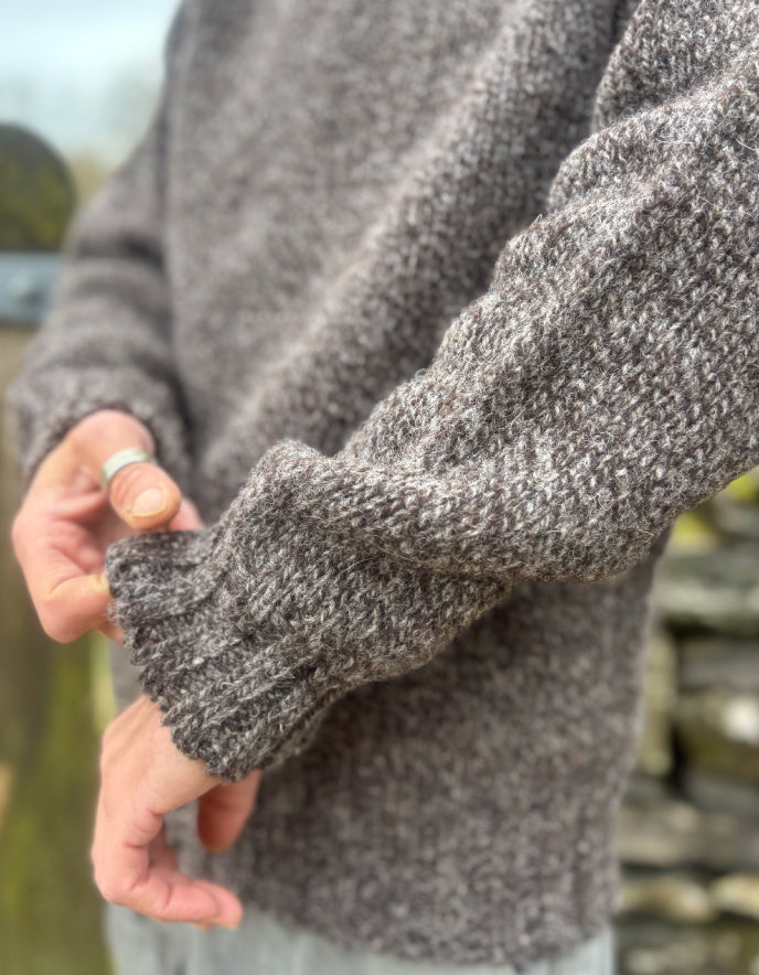 Close-up of a person wearing a textured sweater with a blurred outdoor background