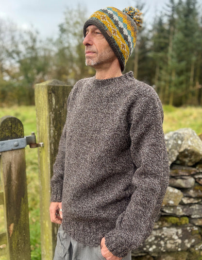 Man wearing a knitted sweater and hat standing by a wooden gate in a natural setting