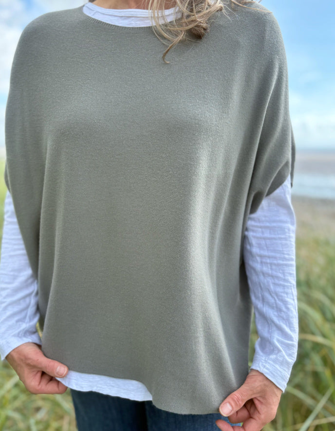 Woman wearing green slate grey tank top with relaxed fit over a white t shirt on a beach and blue sky in the background