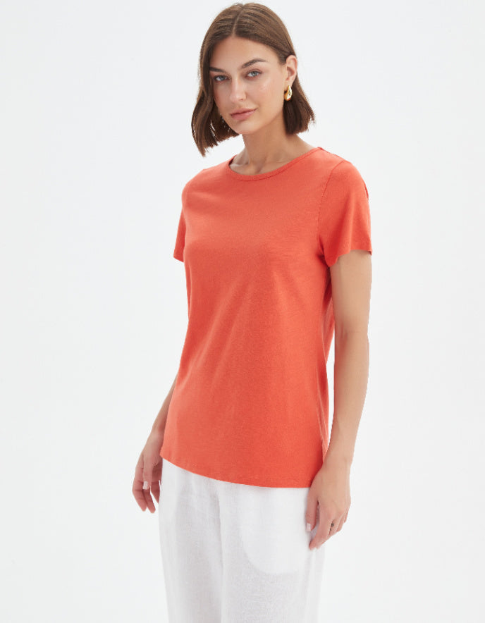 Woman wearing an orange t-shirt and white pants on a light gray background