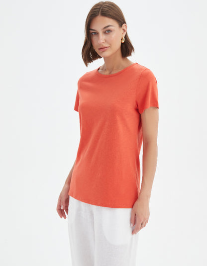 Woman wearing an orange t-shirt and white pants on a light gray background