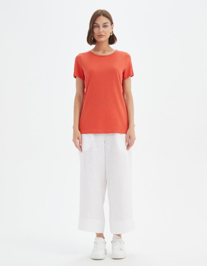 Woman wearing an orange t-shirt and white pants on a white background