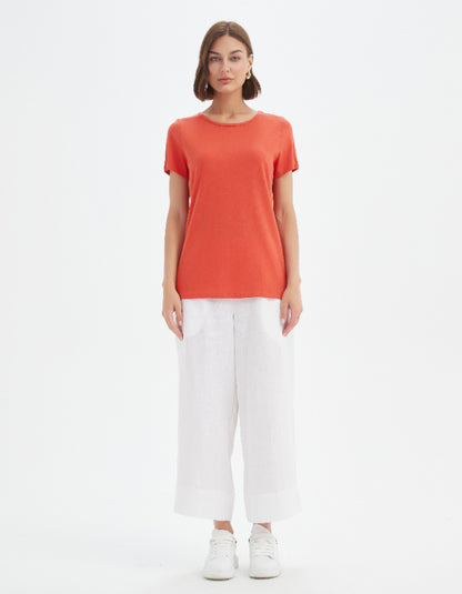 Woman wearing an orange t-shirt and white pants on a white background