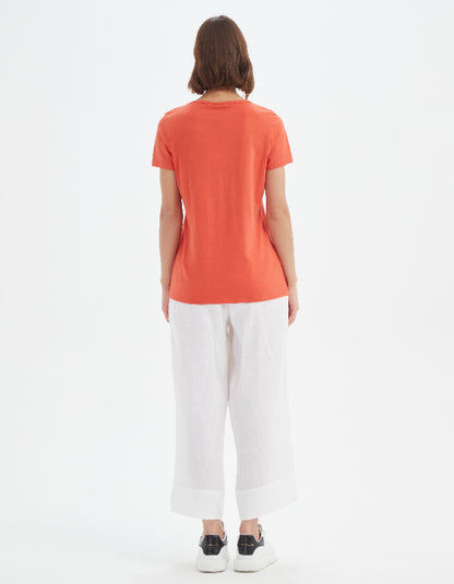 Person wearing an orange t-shirt and white pants on a white background