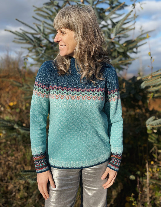 Woman wearing a teal knitted sweater with a patterned design, standing outdoors.