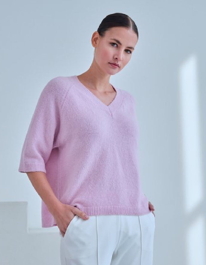 Woman wearing a pink sweater and white pants against a light gray background