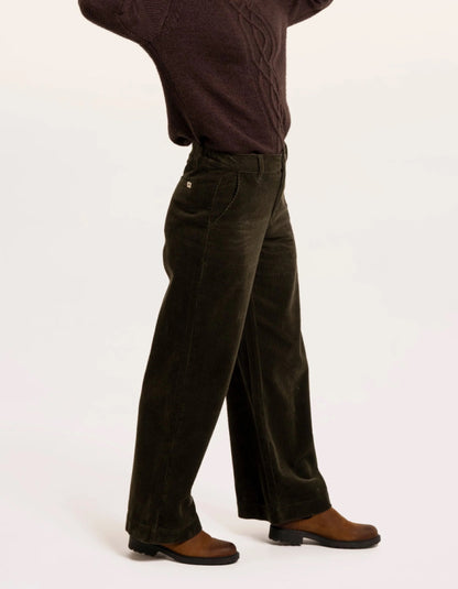 A person shown from the waist down wearing dark olive corduroy trousers, a dark brown sweater, and brown leather shoes against a plain white studio background.