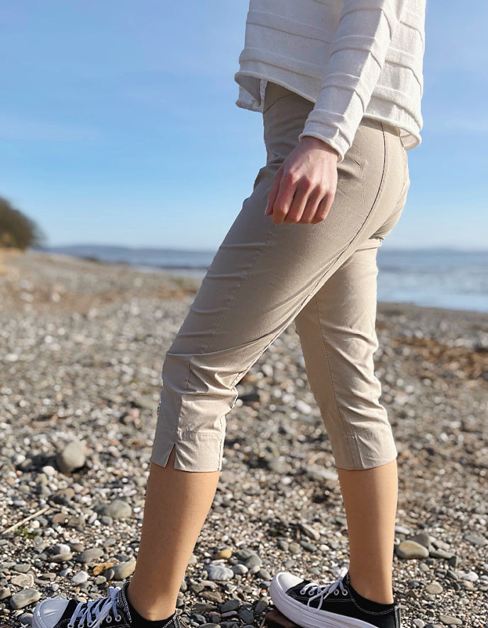 Person wearing beige pants and black sneakers on a pebbly beach with ocean view