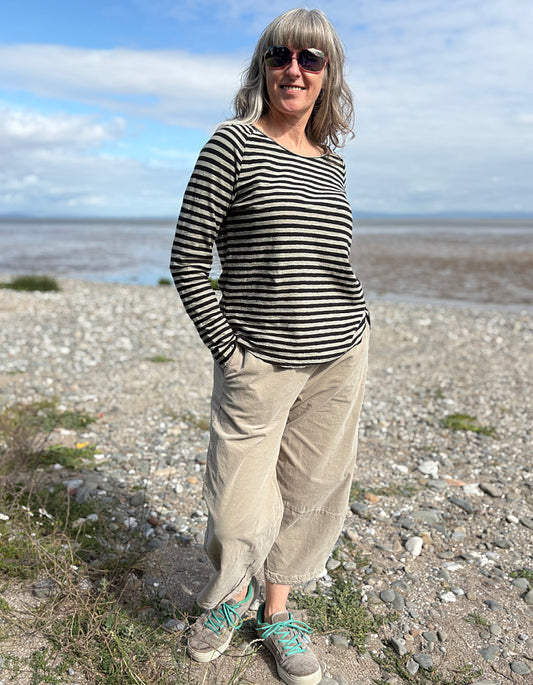 Woman standing on a pebbly beach wearing a striped shirt and sunglasses.