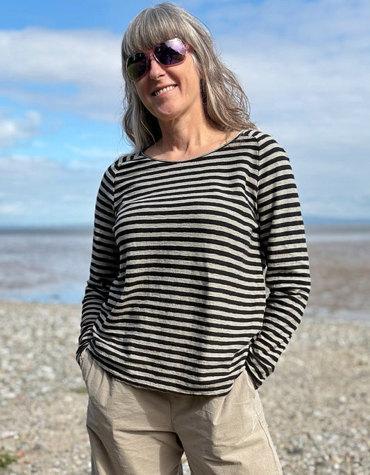 Woman wearing a black and white striped shirt on a beach with a blue sky.