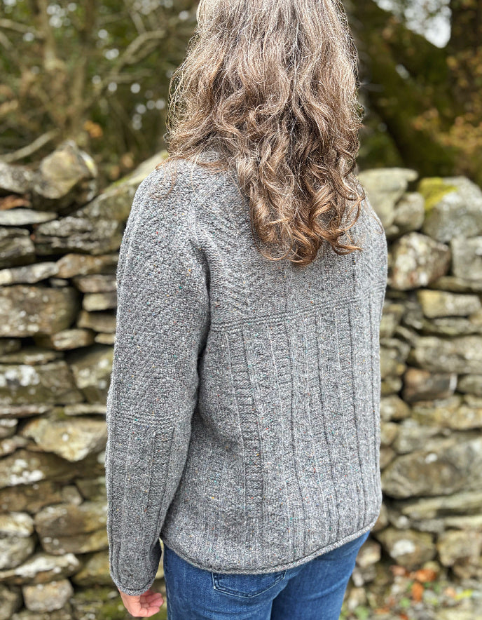 Person wearing a gray knit sweater standing in front of a stone wall