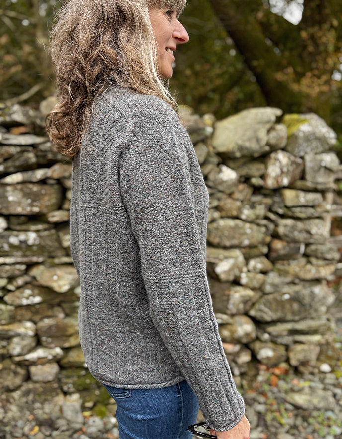 Woman wearing a gray knitted sweater standing in front of a stone wall.