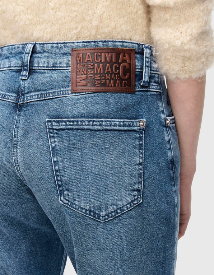 Close-up of blue jeans with a brand label on the back pocket against a neutral background