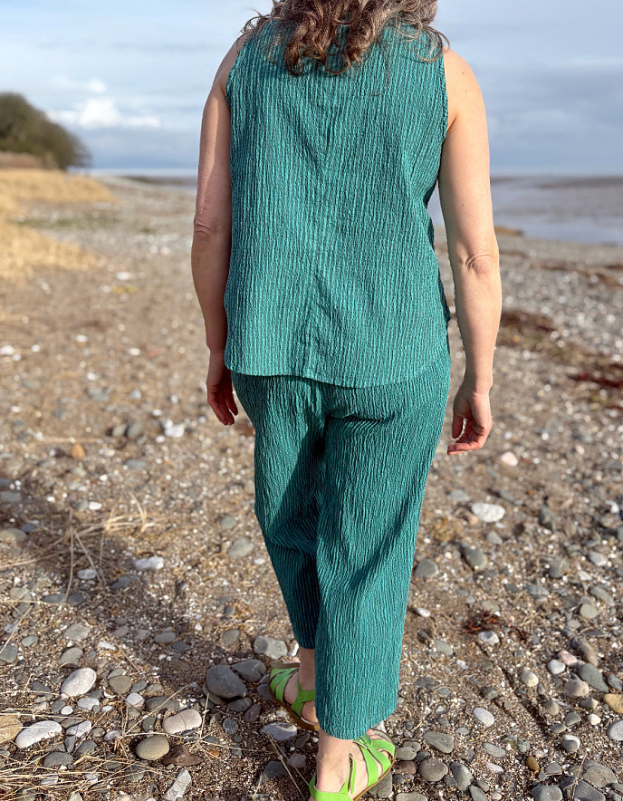 Person wearing a green sleeveless top and pants on a pebbly beach.