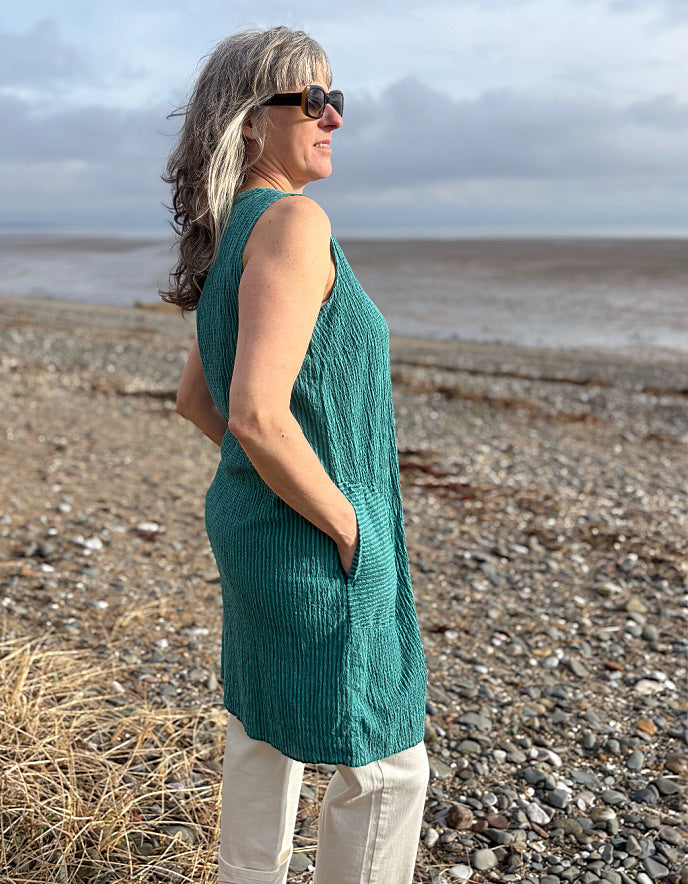 Woman in a green sleeveless top standing on a beach with ocean in the background