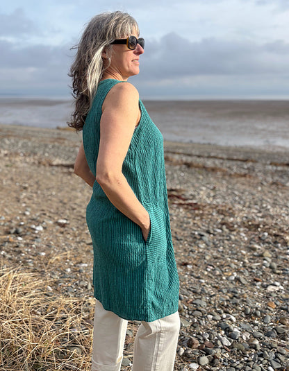 Woman in a green sleeveless top standing on a beach with ocean in the background