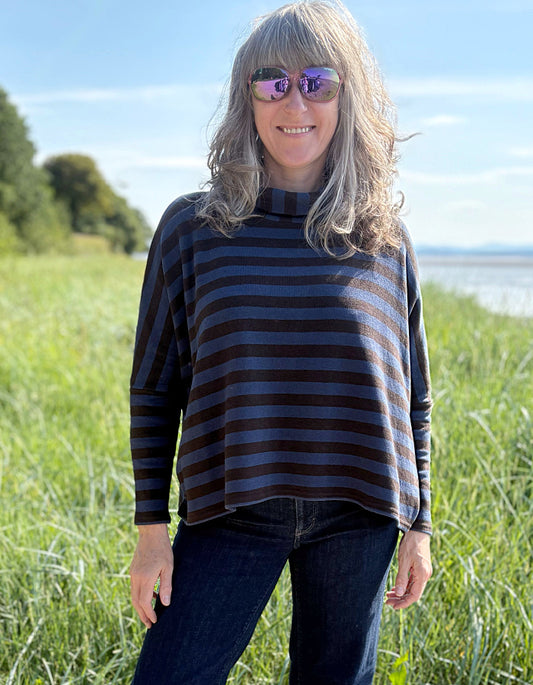 Woman wearing a striped sweater and sunglasses in a grassy field with a clear sky.