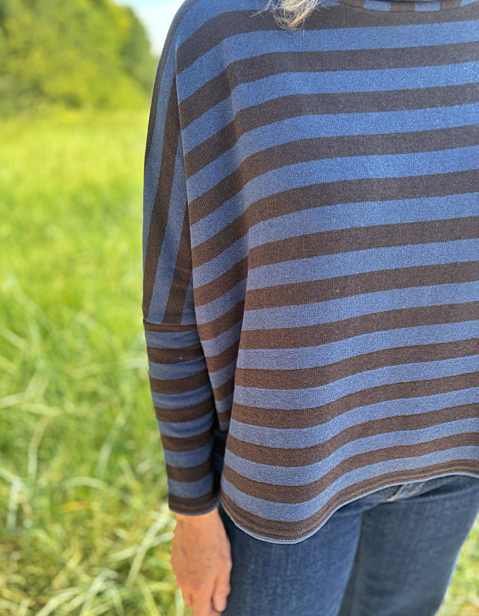 Woman wearing a striped sweater and sunglasses in a grassy field with a clear sky.
