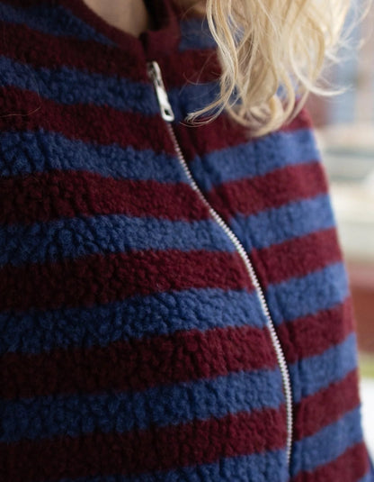 Close-up of a person wearing a fleece zip-up jacket with horizontal burgundy and navy blue stripes, showing blonde hair and the zipper detail.