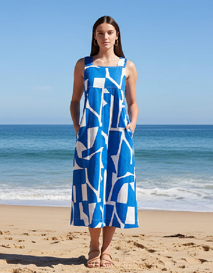 Woman in a blue and white patterned dress standing on a beach with ocean in the background