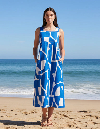 Woman in a blue and white patterned dress standing on a beach with ocean in the background