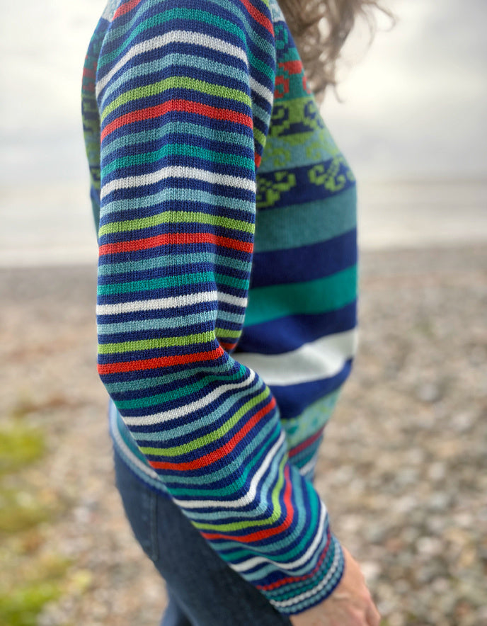 Close-up of a colorful striped sweater sleeve against a blurred natural background