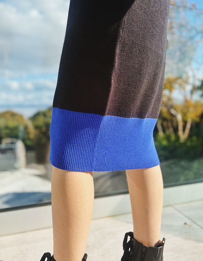 Person wearing a black and blue knit dress with blurred outdoor background