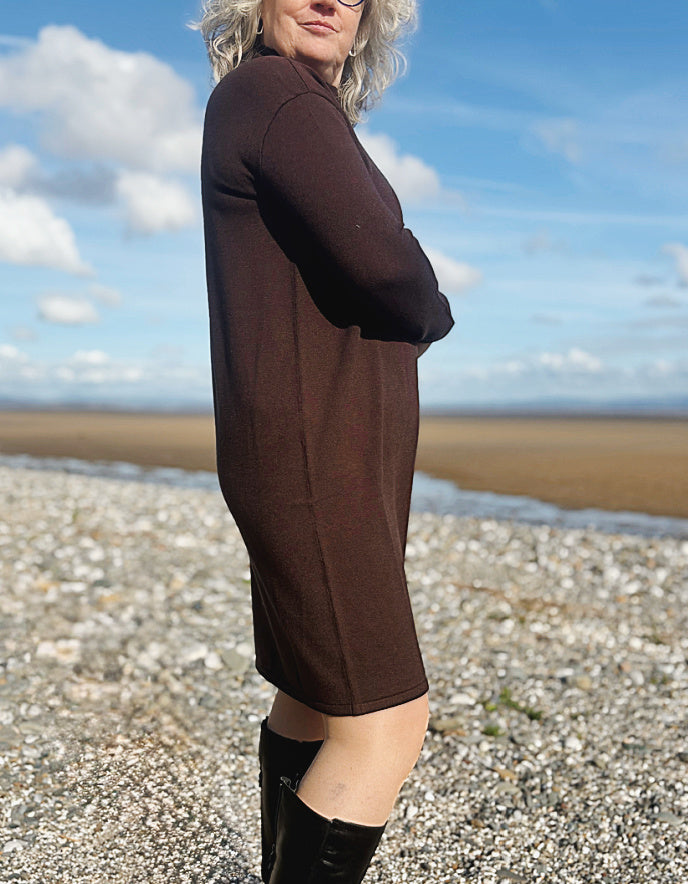 Woman in a brown dress standing on a beach with a blue sky.