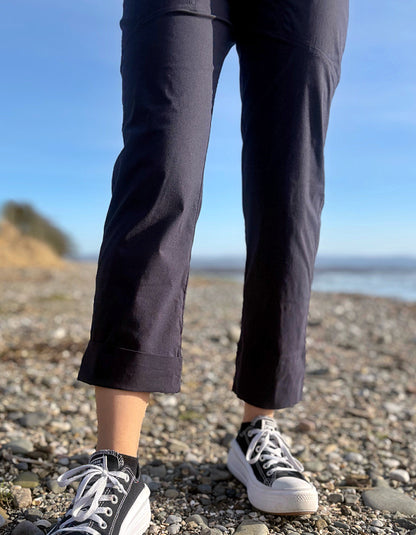 Person wearing black pants and white sneakers on a pebbly beach with a clear blue sky.